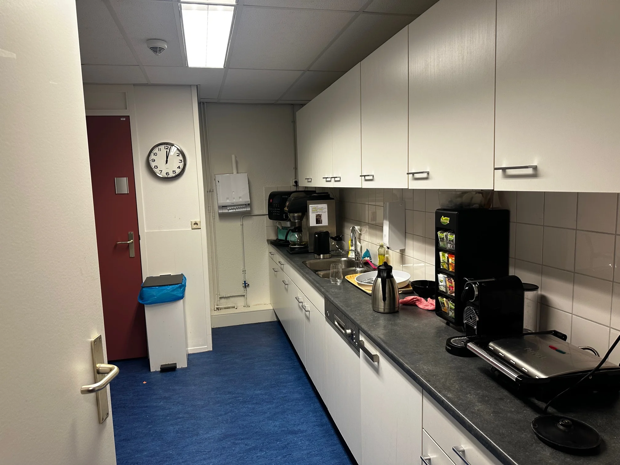 Kleine bedrijfskeuken aan de Van Bleyswijckstraat met koffieapparaten, aanrecht en witte bovenkastjes.